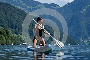 Woman on Summer Alps lake. Sexy young woman paddling on paddle board or sup. Summer vacation in Swiss. Summer lifestyle