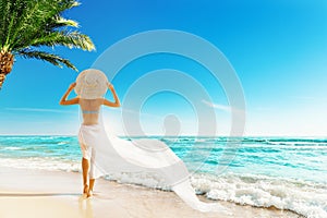 Woman Summer Beach Vacation. Travel Girl Sunbathing in Sun Hat, Bikini, White fluttering Dress. Women Back View looking at Ocean