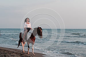 Woman in summer clothes enjoys riding a horse on a beautiful sandy beach at sunset. Selective focus