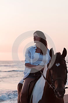 Woman in summer clothes enjoys riding a horse on a beautiful sandy beach at sunset. Selective focus