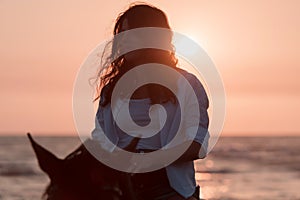 Woman in summer clothes enjoys riding a horse on a beautiful sandy beach at sunset. Selective focus