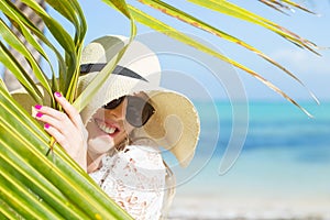 Woman with summer hat on the beach hiding behind palm leaf