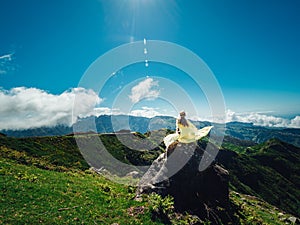 Woman with a summer hat sitting on the rock admitting the stunning landscape of high green mountains photo