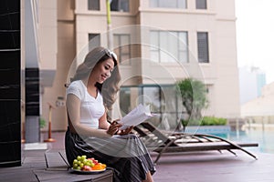 Woman in summer reading a book by the swimming pool. Vacation and relaxation, summer travel concept
