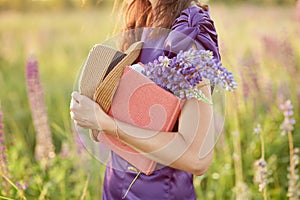 Woman in summer sunset field with bouquet of wildflowers - lupines, hat and pink notebook. Closeness to nature, self