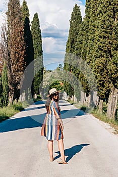 Woman in a sun dress standing on a road surrounded by cypress trees in Tuscany