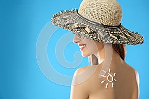 Woman with sun protection cream on her back against blue background. Space for text