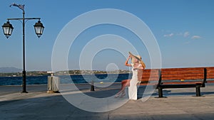 Woman in sun straw hat sitting on a wooden bench on blue sea background at Spetses. Greece