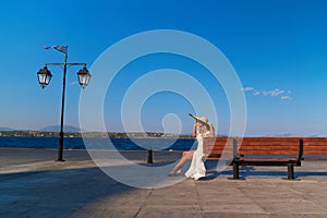 Woman in sun straw hat sitting on a wooden bench at Spetses marina, Greece