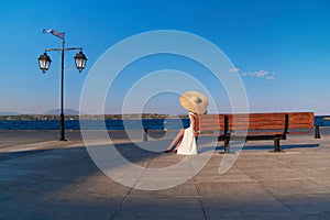 Woman in sun straw hat sitting on a wooden bench at Spetses marina, Greece
