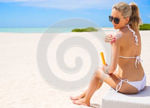 Woman sunbathing on the beach and applying sun protection cream