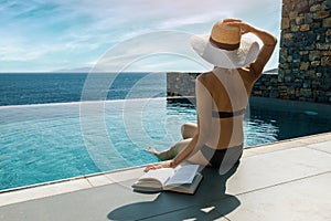 Woman sunbathing and relaxing by the swimming pool with sea view in luxury villa