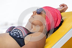 Woman sunbathing and relaxing on yellow sunbed, tanned female with black sunglasses