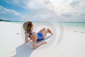 Woman sunbathing on scenic white sand beach, rear view, sunny day, turquoise transparent water, real people. Indonesia, Kei