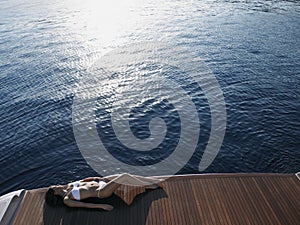 Woman Sunbathing On Yacht's Floorboard By Sea