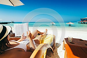 Woman on sunbed reading book under parasol at tropical island