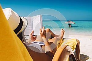 Woman on sunbed reading book under parasol at tropical island