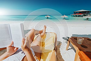 Woman on sunbed reading book under parasol at tropical island