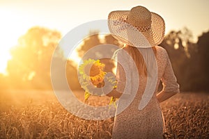 Woman with sunflowers in a retro dress and a hat in a summer wheat field