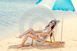 woman in sunglasses and bikini relaxing on beach chair under umbrella