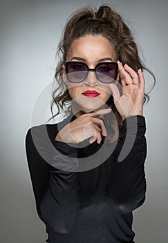 Woman with sunglasses and black blouse against a grey background. Style beauty girl with red lips