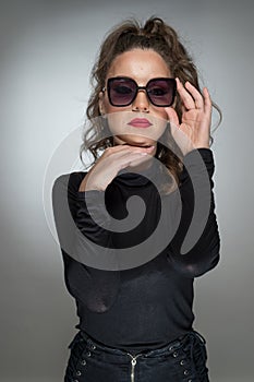 Woman with sunglasses and black blouse against a grey background. Style beauty girl with red lips