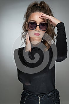 Woman with sunglasses and black blouse against a grey background. Style beauty girl with red lips