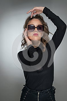 Woman with sunglasses and black blouse against a grey background. Style beauty girl with red lips