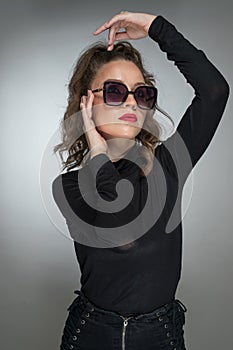 Woman with sunglasses and black blouse against a grey background. Style beauty girl with red lips