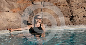 woman with sunglasses and black swimsuit relaxing in spa outdoor swimming pool