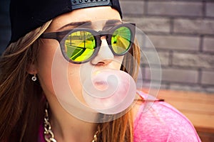 Woman in sunglasses and a cap makes a chewing gum bubble