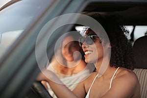 Woman with sunglasses and curly hair driving the car next to a blonde lady