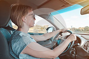 Woman in sunglasses drives modern car and drives on highway. Driver girl sits behind steering wheel of vehicle and looks at road