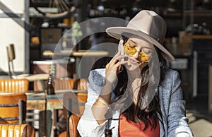 Woman in sunglasses and hat talking on the phone while sitting in a coffee shop