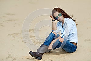 Woman in sunglasses and jeans clothes sitting on a sand - outdoo