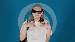 Woman in sunglasses poses in glamour way on blue background