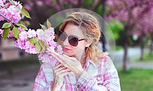 Woman in sunglasses smelling cherry tree blossom