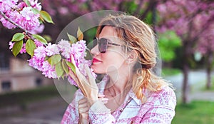 Woman in sunglasses smelling cherry tree blossom profile view