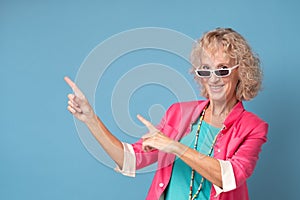 Woman with sunglasses smiling cheerfully and pointing with forefingers away