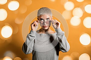 Woman in sunglasses standing near orange bokeh backdrop