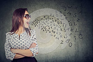 Woman in sunglasses talking with alphabet letters coming out of her mouth.