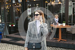 Woman in sunglasses is talking on the phone while her elderly mother is waiting in a cafe