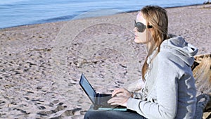 Woman in sunglasses using laptop on the beach