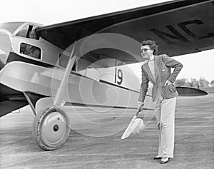 Woman in sunglasses waving a flag on the tarmac next to a airplane