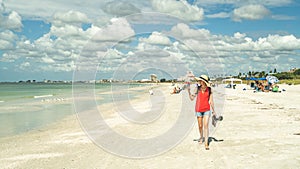 Woman in sunhat and red top walks on beach while using phone