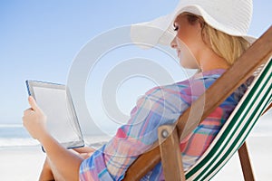 Woman in sunhat sitting on beach in deck chair using tablet pc