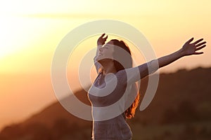 Woman at sunset breathing fresh air raising arms