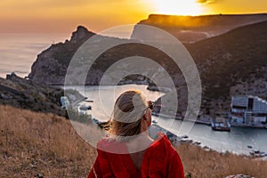 Woman sunset sea mountains. Happy woman siting with her back on the sunset in nature summer posing with mountains on