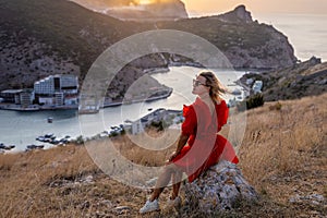 Woman sunset sea mountains. Happy woman siting with her back on the sunset in nature summer posing with mountains on