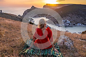 Woman sunset sea mountains. Happy woman siting with her back on the sunset in nature summer posing with mountains on